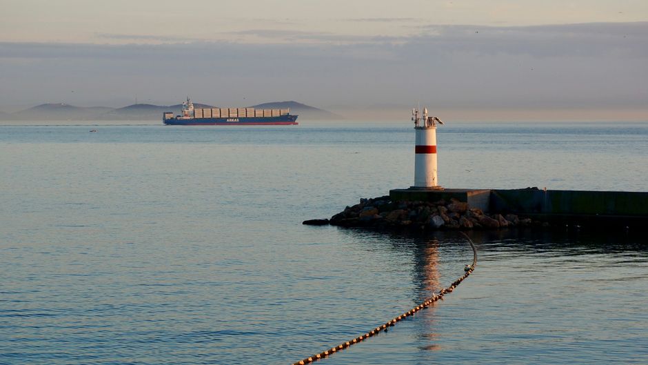 A container ship navigates a strategic strait as geopolitical tensions disrupt energy and global trade routes.