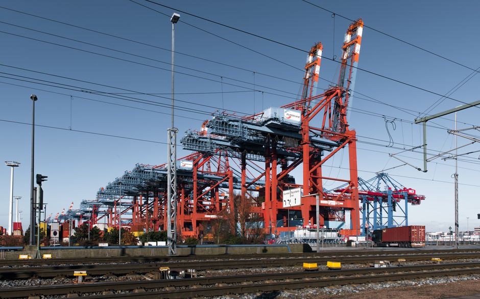 Cranes and stacked shipping containers at a busy container port freight terminal.