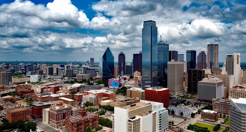 Aerial panoramic view of the Dallas skyline under dramatic clouds, showing the city's cluster of skyscrapers in the financial district.
