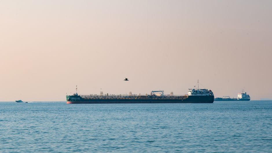 Cargo ships navigating a calm open ocean under a pale sky.