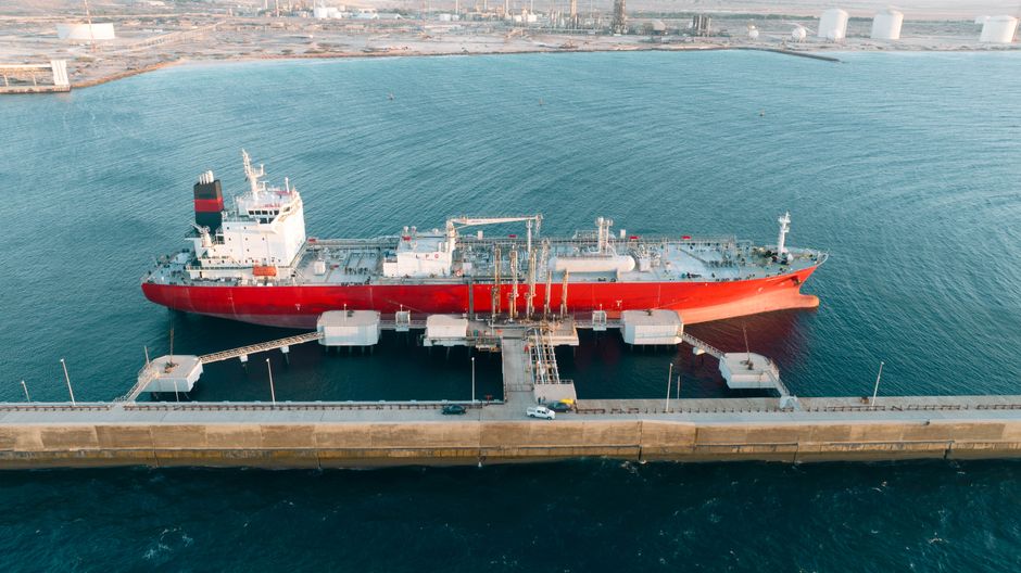 A cargo vessel at an industrial port represents the maritime chokepoints linking energy flows and consumer supply chains.
