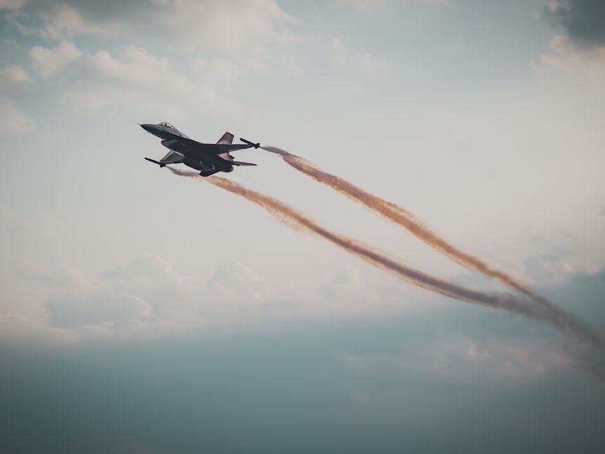 A gray military fighter jet flying through a cloudy sky.