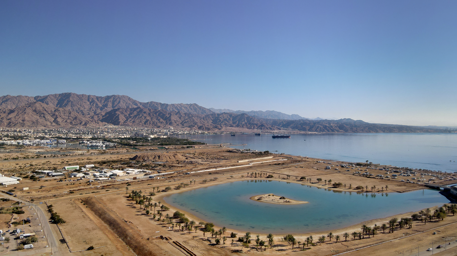 Aerial view of a Middle Eastern coastal lagoon and mountain range, illustrating the strategic geography of the Gulf waterways where the US-Iran ceasefire is now fracturing.