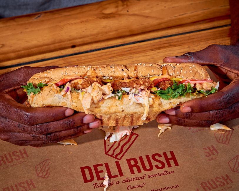Close-up of hands holding a large sub sandwich filled with fresh ingredients at a deli.
