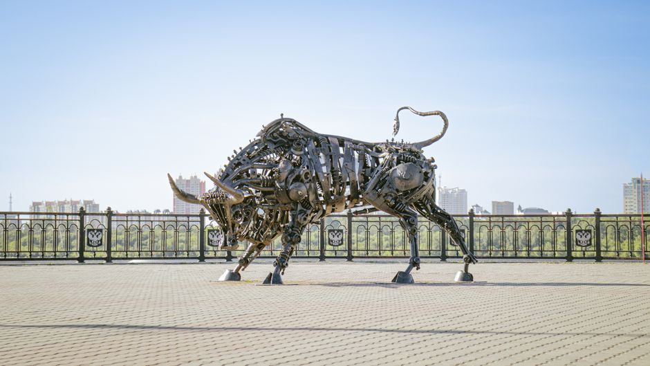 Large bronze bull sculpture standing on a city promenade, symbolizing financial markets and optimism
